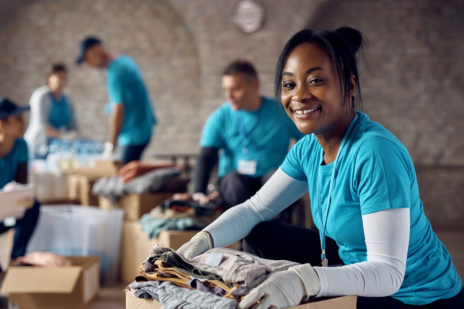 Happy black female volunteer with donation box filled with clothes looking at camera.